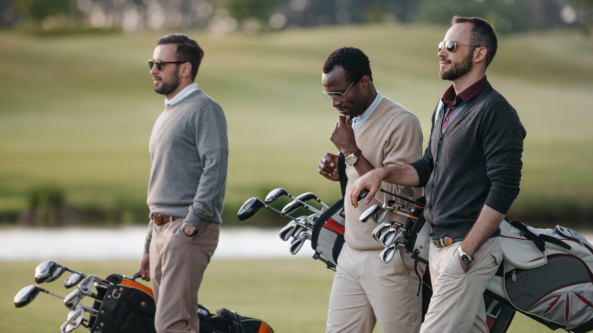 Drei Golfer mit Golftaschen auf dem Platz
